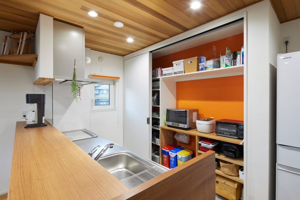対面キッチンには、ビビッドなオレンジ色の壁が印象的な大容量の背面収納を設けた。扉を閉めればLDKをすっきりと見せられる