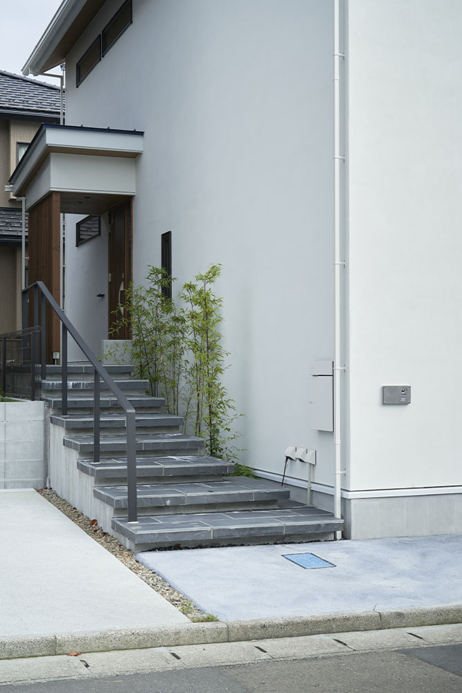玄関までのアプローチは緩やかな階段。踏み板に採用したブラックスレートと、階段脇の植栽が和の佇まいを感じさせる
