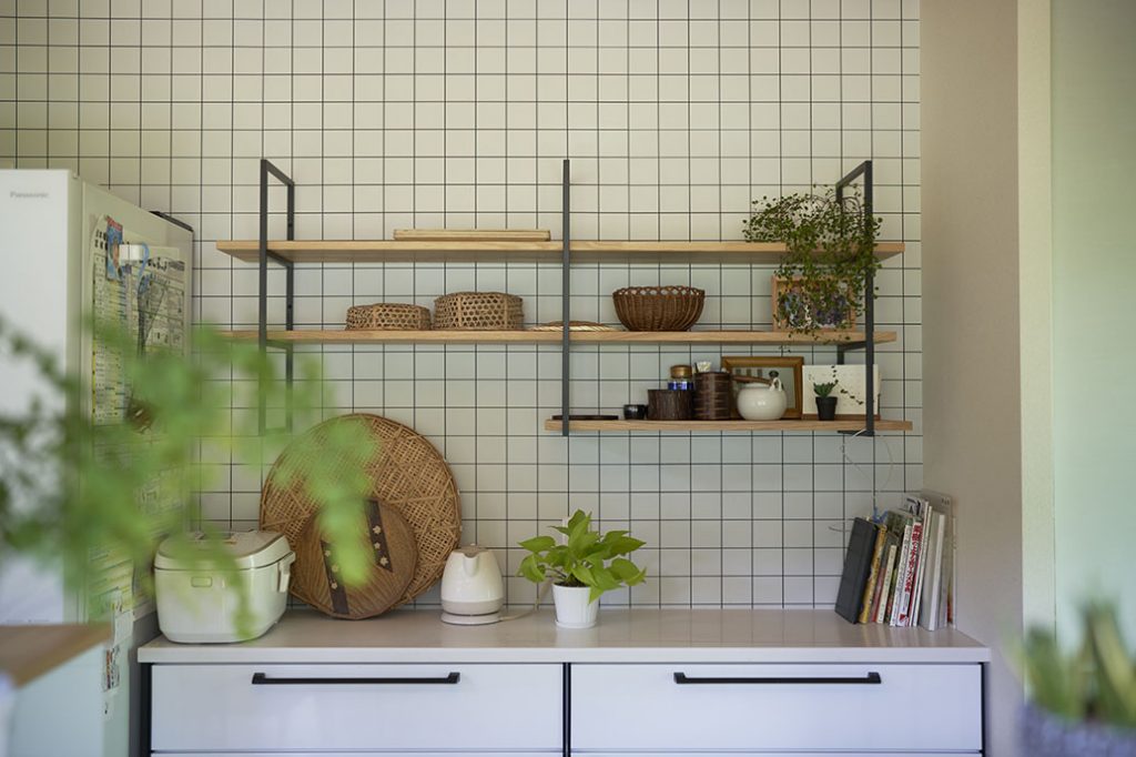 キッチンの背面収納の壁はタイル風の壁紙を張って仕上げ、室内のテイストに合わせた飾り棚を造作
