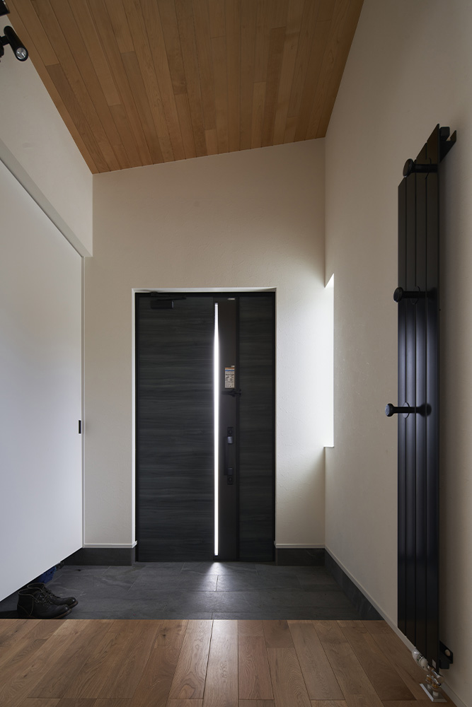 青森ヒバの勾配天井が個性を感じさせる玄関。壁面にはコート掛けにもなるパネルヒーターを設置した