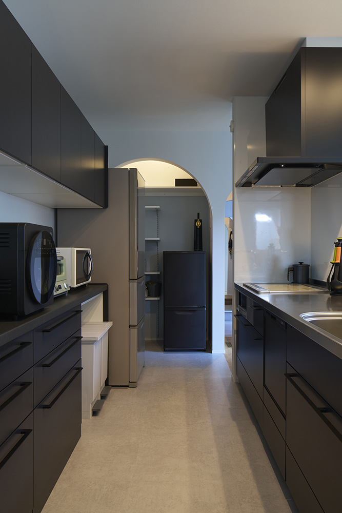 白壁と黒の面材のコントラストが美しいキッチンスペース。システムキッチンは、汚れにくく掃除がしやすいタイプを選択。パントリーとはアール壁でゾーニングしている