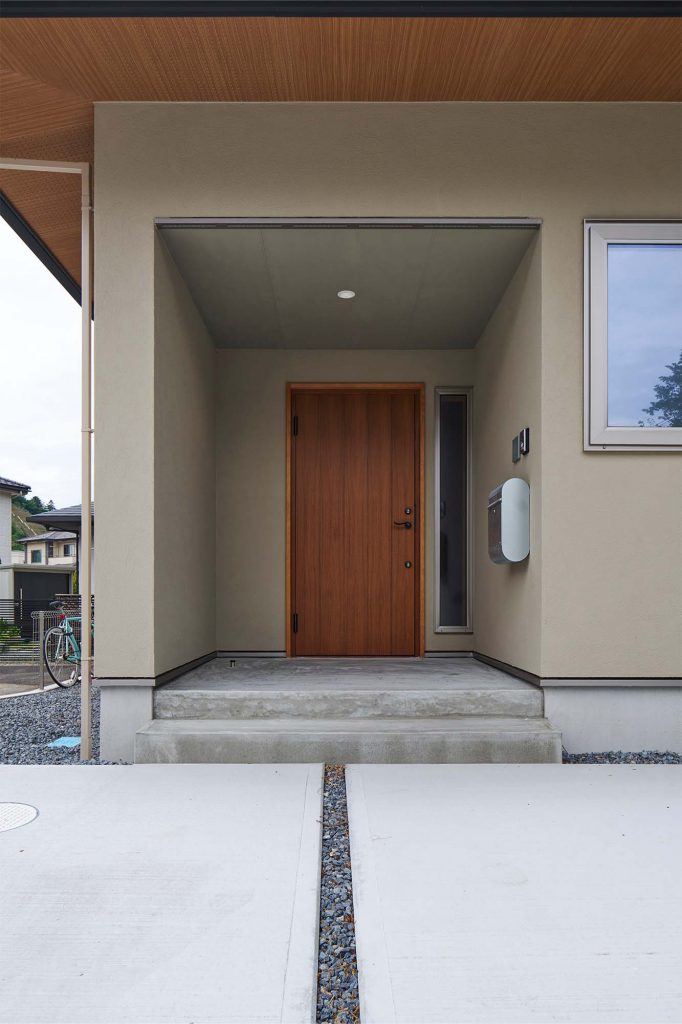 木製玄関ドアと木調の軒天がアクセントに。奥まった玄関は雨の日でも濡れずに出入りできる