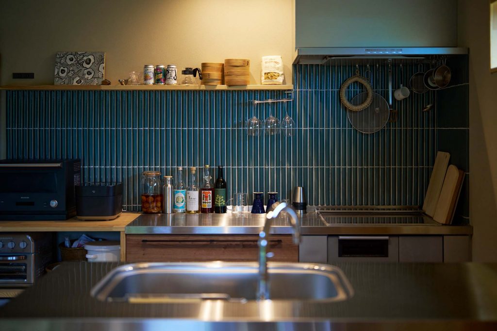 フラットなステンレス天板で使い勝手の良いキッチン。奥さんがチョイスしたネイビーのタイルが空間のアクセントに