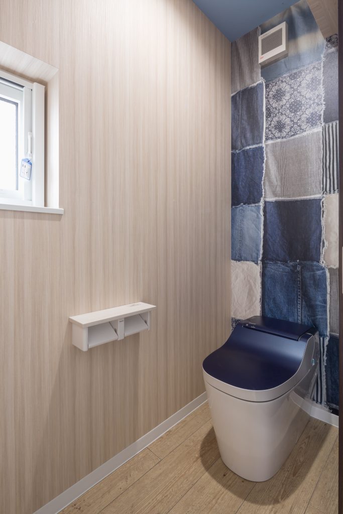 デニム風デザインの壁クロスや便座をブルー系でまとめた個性的なトイレ